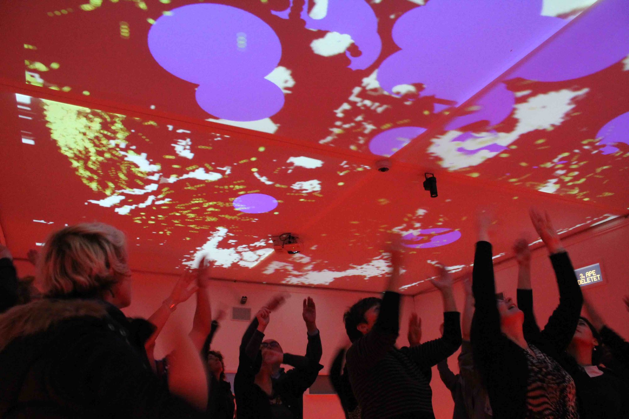 Invisible Treasure, Fast Familiar’s first adventure in multimedia theatre. A group of people in a white box move their arms in the air to control colourful projections on the ceiling. © Cat Lee