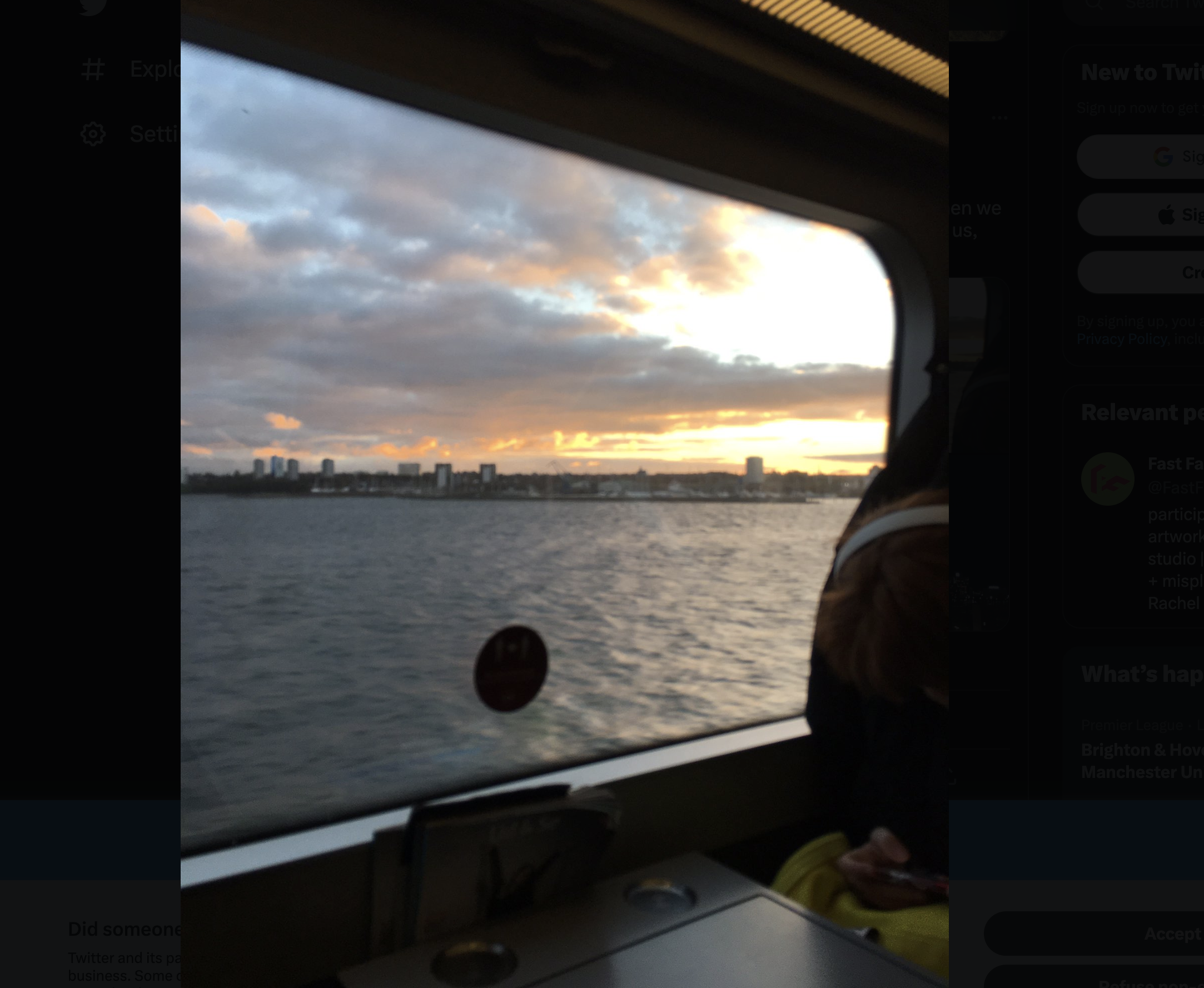 Sunset out of the window of a train, in Denmark. There is a large expanse of water and behind it a city.